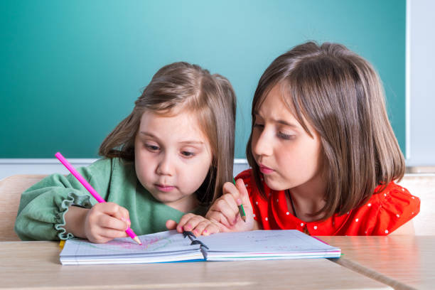 istock older sister looks at her younger sister as she draws in a notebook 1144304161