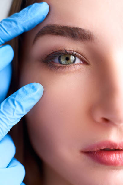 istock Upper eyelid reduction, double eye lid removal plastic surgery concept. Beautician doctor hands in gloves touching female face skin. Ophthalmologist or oculist checks healthy vision in green eyesight 1144306744