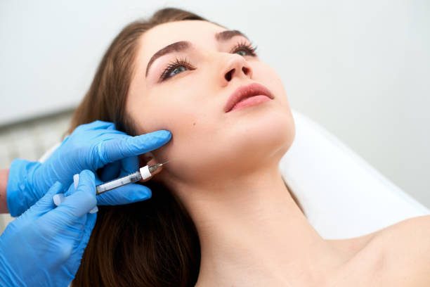 Beautician doctor with filler syringe making injection to jowls. Masseter lines reduction and face contouring therapy. Anti-aging treatment and face lift in cosmetology clinic. Patient lying on chair stock photo