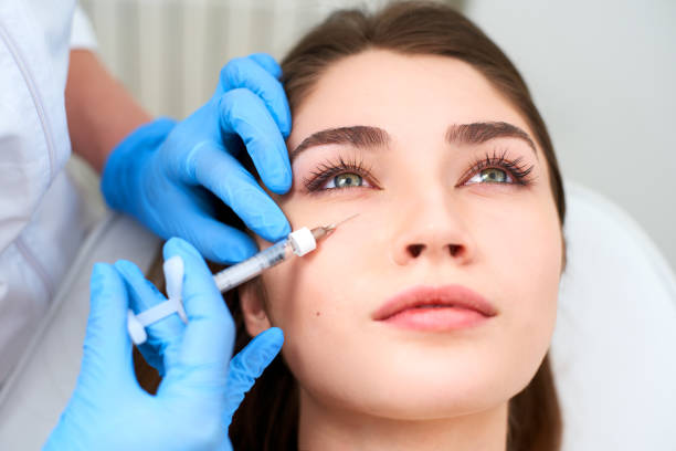 Doctor in medical gloves with syringe injects botulinum under eyes for rejuvenating wrinkle treatment. Filler injection for eye wrinkles smoothing. Plastic aesthetic facial surgery in beauty clinic stock photo