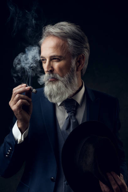 Dapper Gentleman having fashion photoshooting in studio Portrait of Dapper Gentleman on dark background with cigar. Styled, well dressed man. man cigar stock pictures, royalty-free photos & images