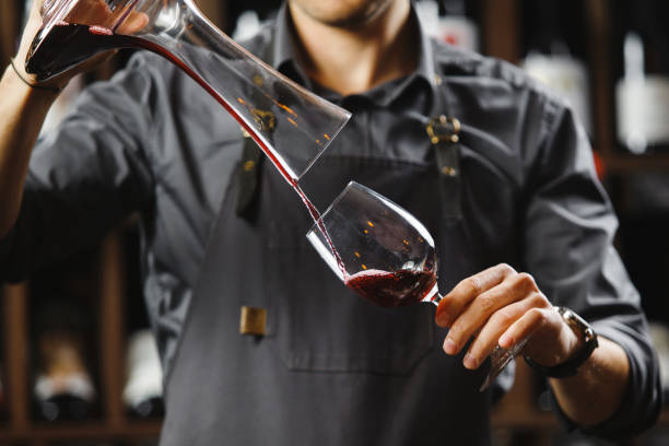 istock Bartender pours red wine in glass from big transparent vessel 1144316938