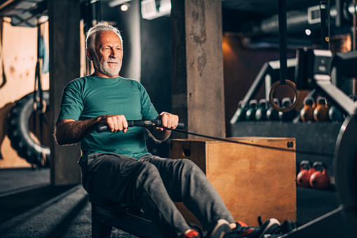 Active elderly sportsman doing a workout on a rowing machine in a gym gym