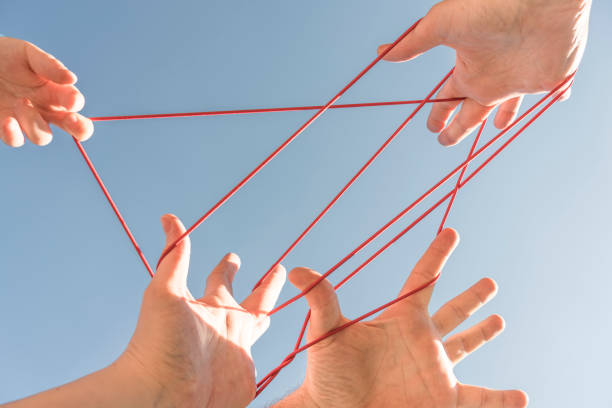 Cats cradle Three adult and one child's hands playing cats cradle against clear blue sky. bridge hand stock pictures, royalty-free photos & images