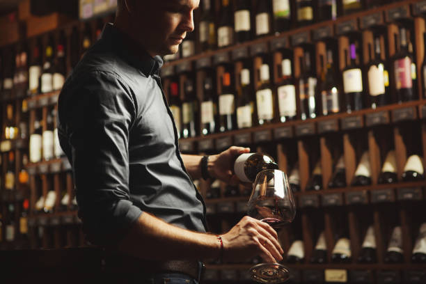 istock Sommelier pouring red wine from bottle in glass on underground cellar background 1144317744