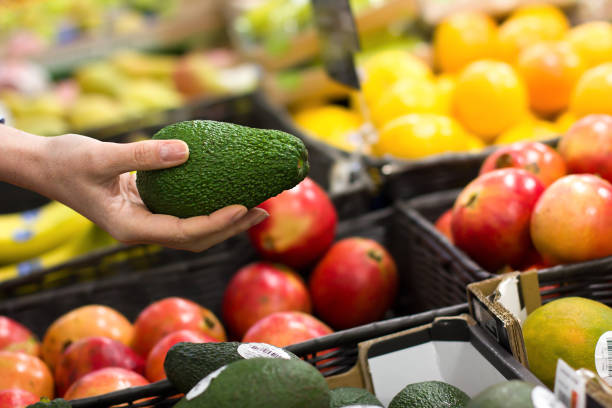 women hand choosing avocado at supermarket - biologic imagens e fotografias de stock