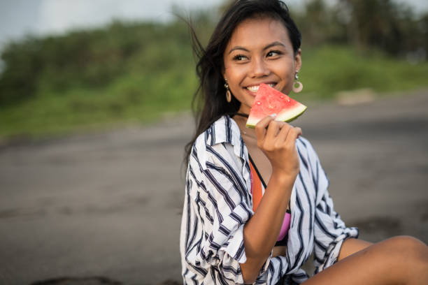 istock Young lady eating watermelon on the beach 1144320522