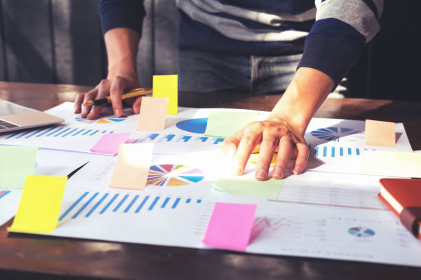 istock Asian business man hand holding note paper meeting working with new startup project use post it notes to share idea discussion and analysis data charts and graphs.Business finances and accounting concept 1144321136