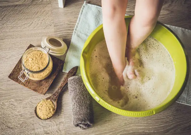 Child taking a healing warming foot bath with mustard powder, adding mustard powder to foot bath with wooden spoon. Against cold illness, aches and improves blood circulation. Alternative medicine.