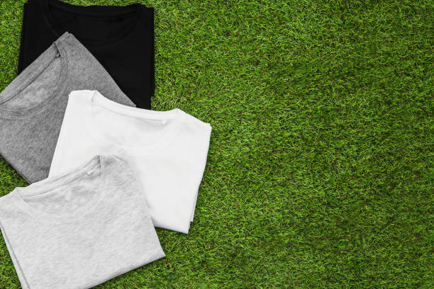 istock Stack of arranged different coloured mens T-shirt on grass background. Horizontal view. 1144328240