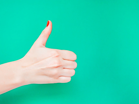 The Thumbs Up Sign. Like Hand Sign. Used when you want to demonstrate that you like something or that you approve of something, The ol thumbs up hand sign. Female hand with red manicure on fingernails holding hand in gesture of likeness giving thumb up on isolated turquoise green color background