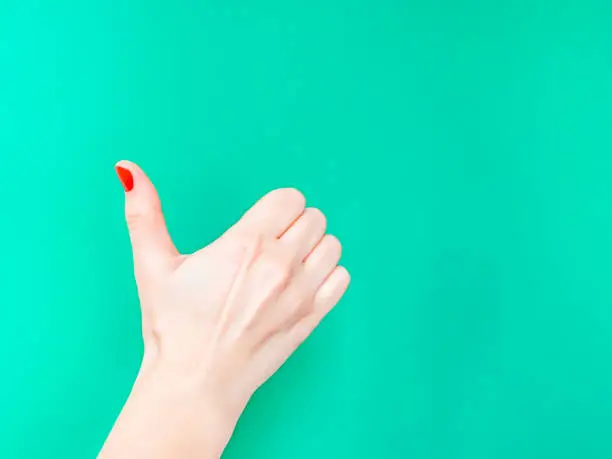 The Thumbs Up Sign. Like Hand Sign. Used when you want to demonstrate that you like something or that you approve of something, The ol thumbs up hand sign. Female hand with red manicure on fingernails holding hand in gesture of likeness giving thumb up on isolated turquoise green color background.