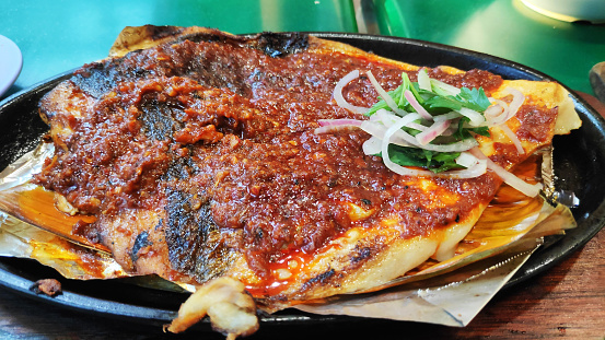 BBQ stingray with spring onions and red chillies paste on a plate