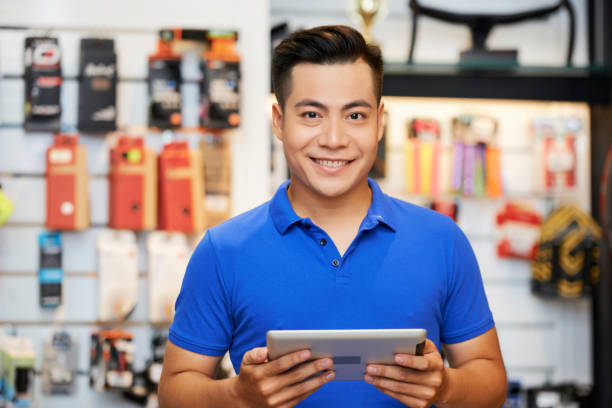 Salesman with tablet pc in the shop Portrait of Asian salesman standing with digital tablet and smiling at camera in workshop salesman stock pictures, royalty-free photos & images