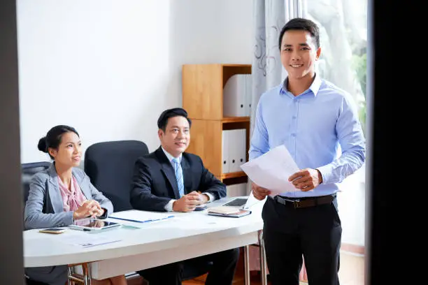 Happy young elegant man with his resume standing in office on background of employers after interview