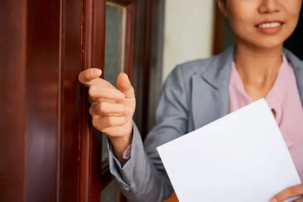 Young elegant female applicant with her resume knocking on wooden door of employer office