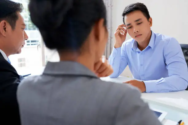 Young pensive applicant keeping hand by temple while thinking of answer during interview