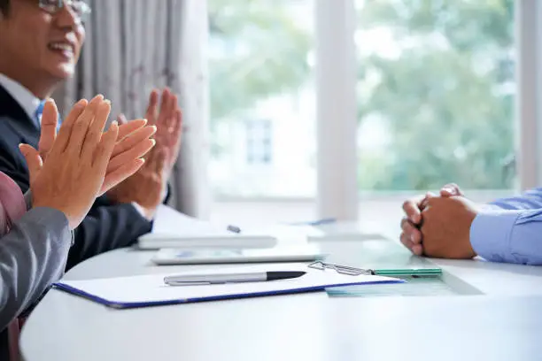 Pen with document and hands of young man on desk and ovations of two mature employers after interview or report