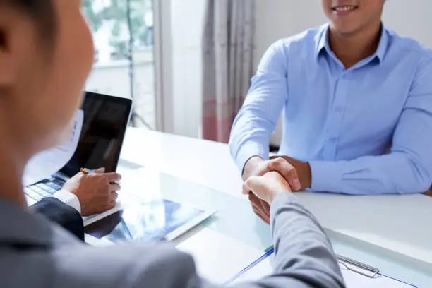 One of employers shaking hand of young applicant after successful interview while congratulating him on new job