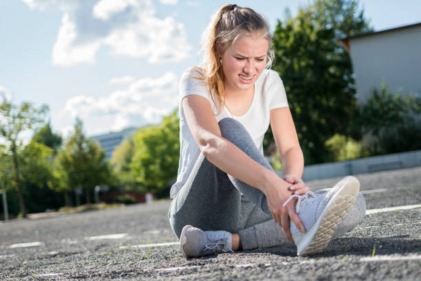 A young woman has injured her ankle while exercising A young woman has injured her ankle during sports and holds her foot sprain stock pictures, royalty-free photos & images