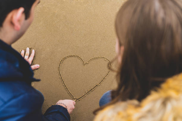 Young couple in love paints a heart in the sand on the beach