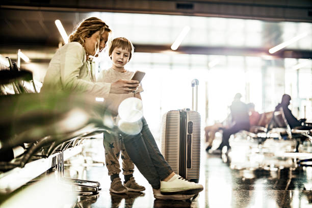 istock Mother and son using cell phone while waiting for their transportation at departure area. 1144345474