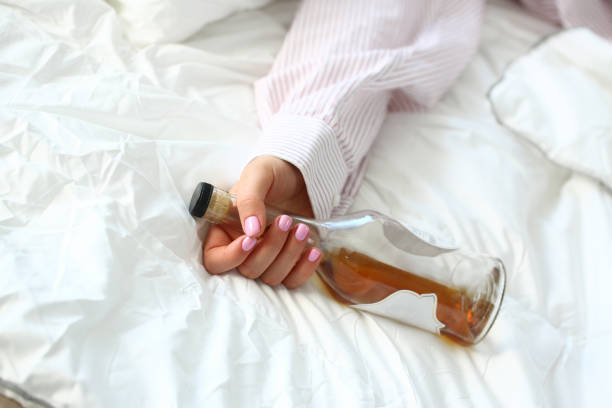 Young woman lying in bed deadly drunken Young woman lying in bed deadly drunken holding near-empty bottle of booze. Female intoxicated with alcohol after tough night party. Alcoholism habitual drunkenness pernicious habit concept alcoholism alcohol addiction drunk stock pictures, royalty-free photos & images