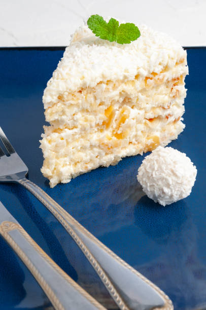 istock A piece of white cake with almonds and coconut chips on a blue plate. Decorated with mint and candy with coconut. 1144347741