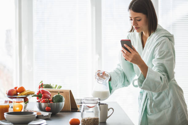 istock Woman in bathrobe holding smart phone and preparing breakfast in the kitchen 1144347826