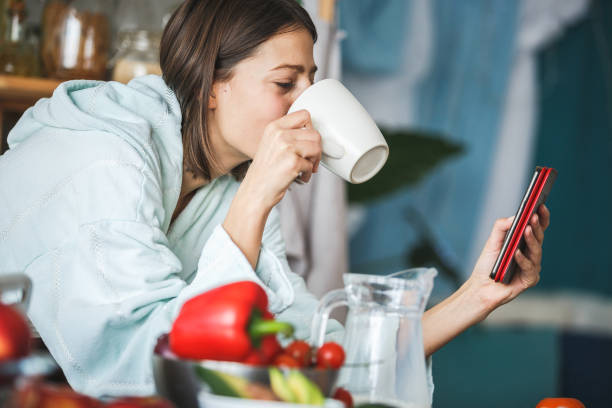 istock Woman drinking coffee and using smart phone in the kitchen 1144347838