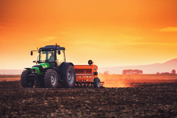 istock Farmer with tractor seeding crops at field on sunset 1144351056