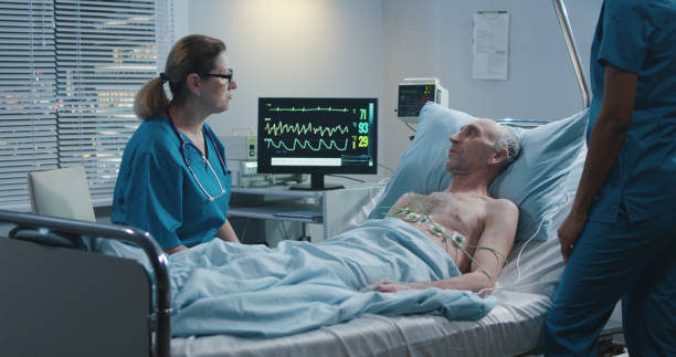 Doctor talking with patient Medium shot of a female doctor talking with an elderly male patient after putting ECG cables on him night hospital bed stock pictures, royalty-free photos & images