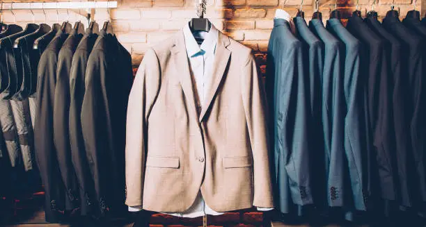 Men formal wear. Classy outfit. Modern clothing store. Business suit jackets and vests hanging, displayed over brick wall.