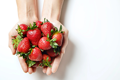 Ripe local produce organic strawberry. Young woman holding heap of red berries in bare hands. Fresh healthy vegan dietary food for spring detox. Fruits background, top view. Clean eating concept.