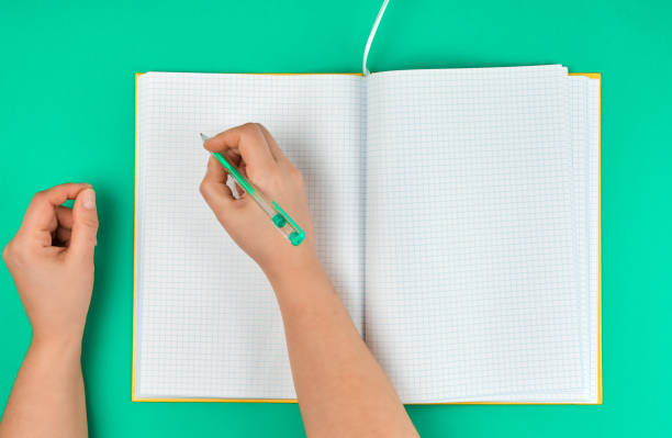 istock female hand holding pen, near  blank open notebook in a cell 1144370245