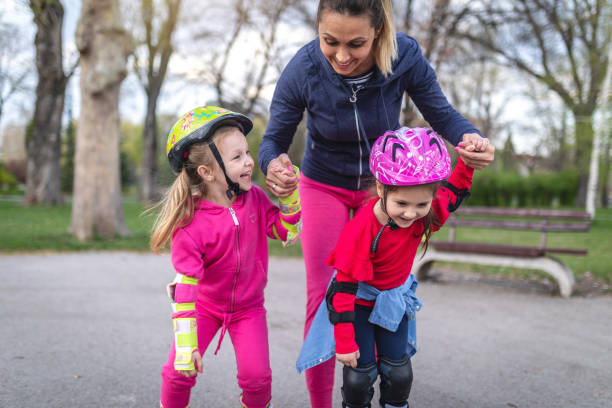 Mother with daughters in the park. One of them fell from rollerblades while woman is consoling her.