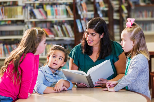 istock Hispanic teacher and three girls in library reading book 1144373791