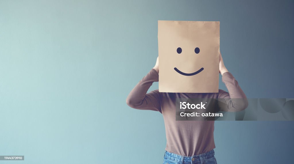 Woman covering his face with a smiling face emoticon, copy space. Hiding Stock Photo