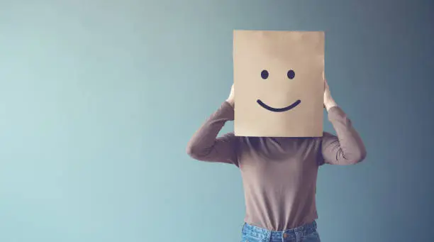 Photo of Woman covering his face with a smiling face emoticon, copy space.