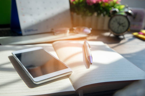 Diary and smartphone for planning work schedules and appointments.Desktop laptop,calendar,clock,diary,books and glasses on wooden desk,Working space at home.Lifestyle concept