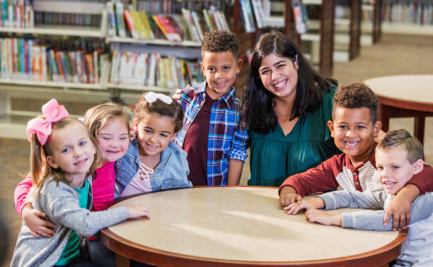 professeur hispanique, enfants d’école élémentaire dans la bibliothèque - arm around caucasian latin american and hispanic ethnicity child photos et images de collection