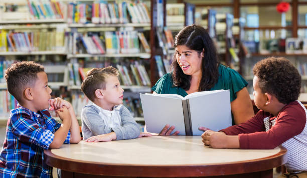 istock Hispanic teacher with three boys in library reading book 1144374491
