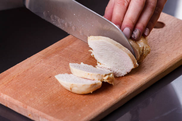 young woman in a gray apron cuts chicken breast.