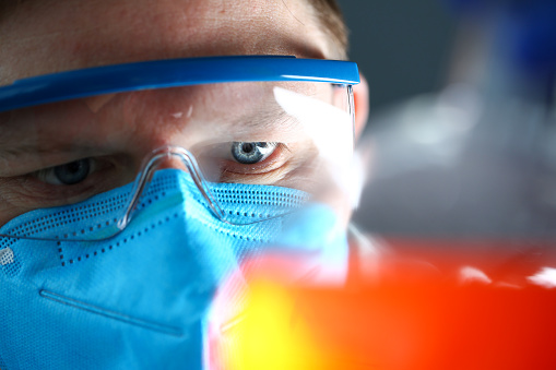 Laboratory man wearing protective mask hold in hand test sample closeup