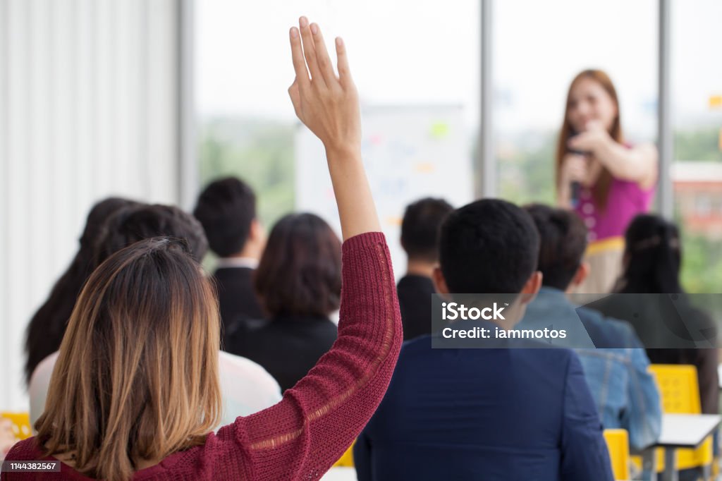 young businesswoman raising hand  to question from Speaker in Seminar. Group Meeting . Conference  Concept . Rear back view Hand Raised Stock Photo