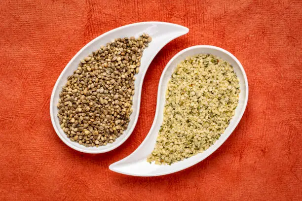 dry hemp seeds and hearts in small teardrop bowls against orange textured paper