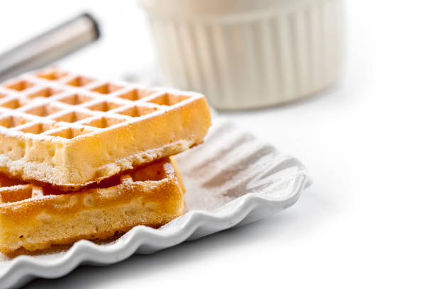 Belgium waffers with sugar powder on ceramic plate and strainer on white table. Fresh baked wafers.