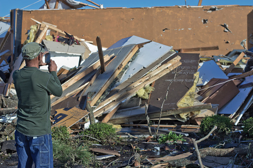 Fayetteville, NC, USA - April 17, 2011: African american man photographs a tornado damaged business with his cell phone. The structure was destroyed by a tornado the previous day. This event is the most significant tornado even in North Carolina in twenty to thirty years. The severe weather damaged hundreds of homes, businesses, and government buildings across the state, prompting national attention and the governor to declare a state of emergency.