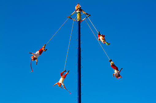Puerto Vallarta, Mexico: The Flyers of Papantla (Volardores de Papantla) perform in the vibrant blue sky of downtown Puerto Vallarta for tourists. The performance, where men hang upside down from ropes, has been granted UNESCO cultural heritage status. Plenty of copy space in the sky.