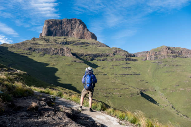 Admiring the mountains in the Drakensberg A man on a hike in the Drakensberg Mountains, stops on the hiking trail and admires the view of the mountains. He has a large blue hiking bag drakensberg mountain range stock pictures, royalty-free photos & images